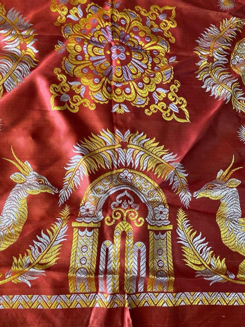May include: Red fabric with gold, silver, and yellow embroidered patterns. The design includes floral motifs, archways, and deer-like creatures. The fabric has a shiny, textured appearance.