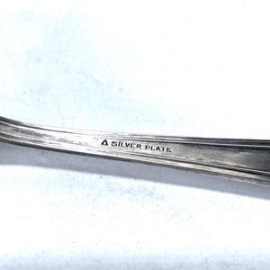 May include: Close-up of a silver-plated utensil, possibly a fork or spoon, with a curved handle. The text "A SILVER PLATE" is stamped on the handle. The utensil has a shiny, reflective surface.