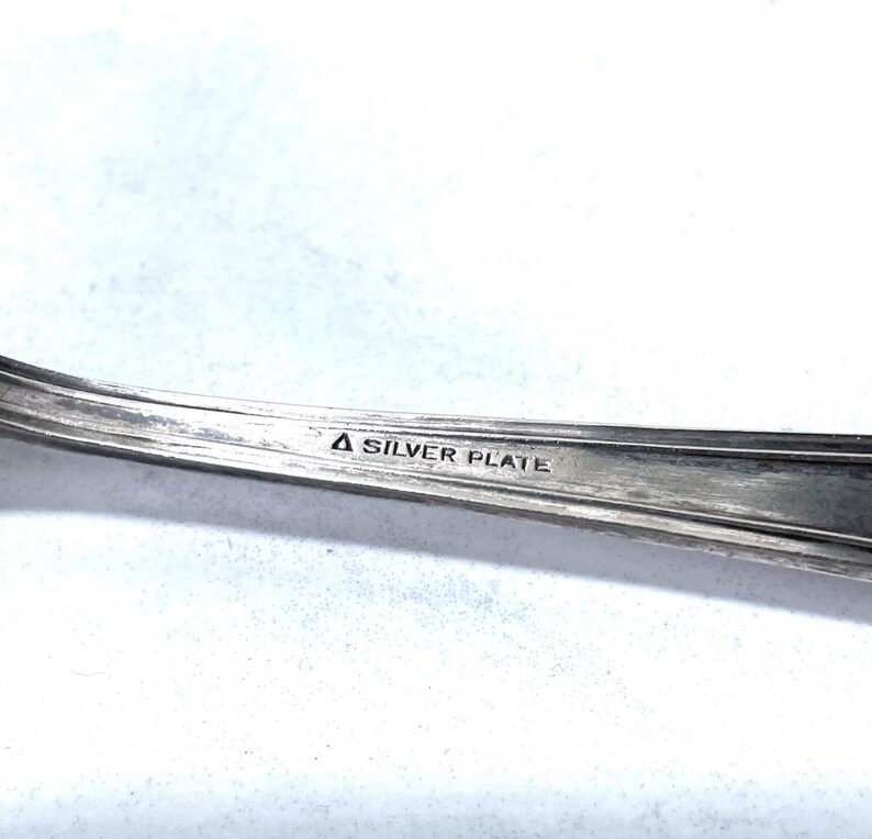 May include: Close-up of a silver-plated utensil, possibly a fork or spoon, with a curved handle. The text "A SILVER PLATE" is stamped on the handle. The utensil has a shiny, reflective surface.