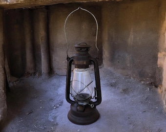 May include: A vintage, dark brown lantern with a clear glass globe and a metal handle. The lantern has a round base and a cylindrical body. The handle arches over the top. The lantern is sitting on a stone surface.