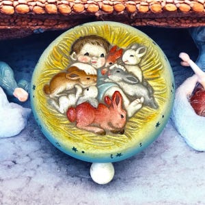 May include: A round, ceramic ornament featuring a baby surrounded by several rabbits. The baby has brown hair and is smiling. The rabbits are in shades of brown, white, and red. The ornament has a yellow and blue background with small star details.