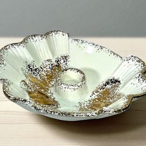 May include: A vintage ceramic centerpiece bowl with a scalloped edge and a central candle holder. The bowl is light green with gold leaf accents and a speckled gold and black trim. The design is reminiscent of a seashell.