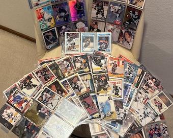 May include: A collection of hockey trading cards, many in protective sleeves, featuring various players in action. The cards showcase different teams and designs, with a variety of colors and action shots. Some cards are displayed in clear plastic sheets.