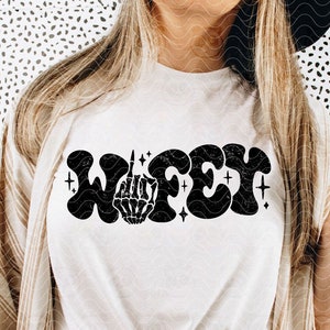 May include: A white t-shirt with a black graphic that says "WIFEY" in a retro font. The graphic includes a skeleton hand giving the middle finger.