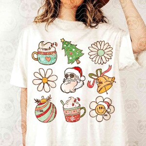 May include: A white t-shirt featuring a collection of colorful Christmas-themed graphics. Designs include a dog in a mug, a Christmas tree, daisies, Santa Claus, a bell, and a smiling flower. The shirt has the text "DIGITAL DOWNLOAD PNG DISTRESSED & SOLID PNGS".