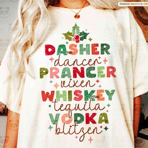 Puede incluir: Camiseta color crema con un diseño de árbol de Navidad hecho con texto colorido. Las palabras "DASHER, dancer, PRANCER, vixen, WHISKEY, tequila, VODKA, blitzen" están dispuestas en forma de árbol, con un diseño de acebo y bayas.