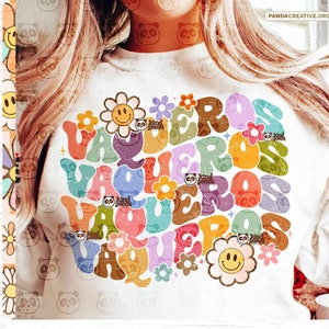 May include: A white t-shirt with a colorful graphic design of the word "VAQUEROS" in a retro style with flowers and smiley faces.