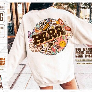 K&ouml;nnte beinhalten: Ein wei&szlig;er Pullover mit einem braunen und farbenfrohen Grafikdesign, das das Wort "PARRA" zeigt, umgeben von Blumen, Schmetterlingen und anderen skurrilen Elementen. Das Design ist im Retro-Stil der 70er Jahre.