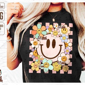May include: Black t-shirt with a large smiley face design surrounded by flowers in pastel colours. The design includes the text "kind panda studio" and a checkered background. Digital download option.
