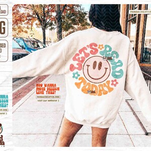 Puede incluir: Una sudadera blanca con un dise&ntilde;o gr&aacute;fico colorido que dice "Let's be rad today" con una carita sonriente en el centro. El dise&ntilde;o es de estilo retro con un esquema de colores arco&iacute;ris.