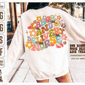 May include: A white sweatshirt featuring a colourful graphic design that reads "Labor and Delivery Nurse" in a retro style. The design incorporates flowers, stars, and a smiley face. The text "You wanna more design like this? Pandacreative.org visit our website :)" is at the bottom of the image.