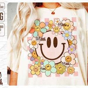 May include: A cream-coloured t-shirt with a large smiley face design surrounded by colourful flowers. The smiley face and flowers have a retro, distressed look. The shirt has a checkered background and the text "kind panda studio".