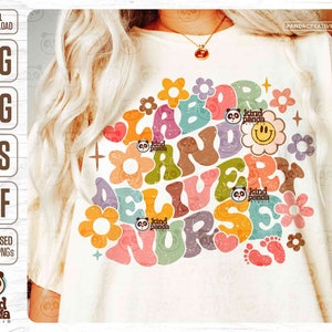 May include: A white t-shirt featuring a colourful graphic design that reads "Labor and Delivery Nurse" in a retro style with flowers and a smiley face. The design also includes the text "Kind Panda Studio".