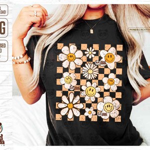 May include: A black t-shirt with a checkered pattern in orange and white. The pattern is filled with white daisies with yellow centers and smiley faces. The text "be kind panda" is written in a circle on some of the daisies.