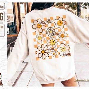 K&ouml;nnte beinhalten: Ein wei&szlig;es Sweatshirt mit einem karierten Muster und gelben G&auml;nsebl&uuml;mchen mit Smiley-Gesichtern. Die G&auml;nsebl&uuml;mchen haben den Text "go kind panda" auf sich.