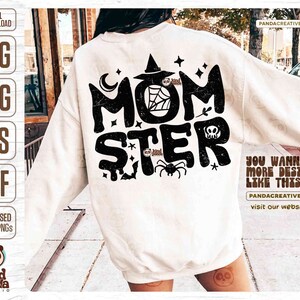 May include: A white sweatshirt with a black distressed graphic that says "Momster" with a spider, a witch's hat, a crescent moon, and a skull. The text "You wanna more design like this?" is on the right side of the sweatshirt.