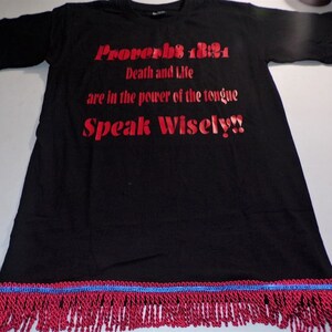 Könnte beinhalten: Schwarzes T-Shirt mit rotem Aufdruck "Sprüche 18:21 Tod und Leben sind in der Macht der Zunge Sprich weise!!" Das Shirt hat einen roten und blauen Fransenbesatz.