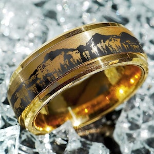 May include: A gold tungsten carbide ring with a black mountain range design engraved on the band.