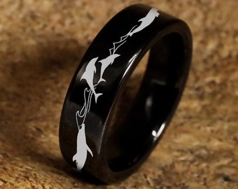 May include: A black tungsten carbide ring with a white dolphin design engraved around the band.