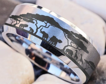 May include: A silver ring with a black band featuring an engraved design of a savanna landscape with trees and animals.