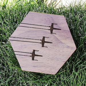 May include: A hexagonal wooden coaster with a dark wood stain. The coaster features a design of five silhouettes of X-Wing starfighters.