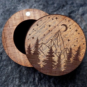 May include: A round wooden box with a hinged lid. The lid features a laser-engraved design of a mountain range with trees and a crescent moon in a starry night sky.