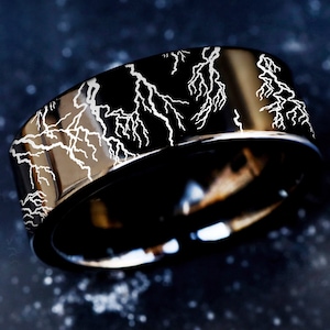 May include: A black tungsten carbide ring with a white lightning bolt design.
