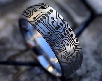 Könnte beinhalten: Ein silberner Ring mit einem schwarzen Schaltkreisdesign. Der Ring ist aus Wolframcarbid gefertigt und hat eine gebürstete Oberfläche.