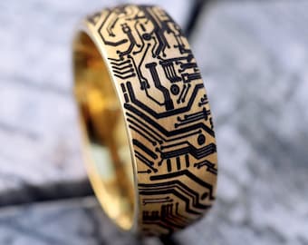 Könnte beinhalten: Ein goldener Ring mit einem schwarzen Schaltkreisdesign. Der Ring ist aus Metall und hat eine polierte Oberfläche.