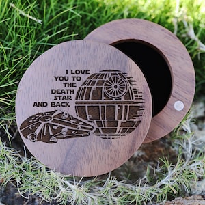 May include: A wooden ring box with a laser engraved design of the Millennium Falcon and the Death Star. The lid of the box has the text "I love you to the death star and back".