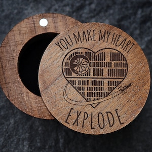 May include: Wooden ring box with a heart-shaped design and the text "You make my heart explode". The heart is a stylized image of the Death Star from Star Wars.