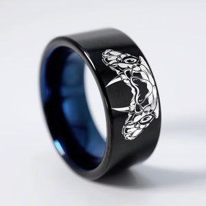 Könnte beinhalten: Ein schwarzer Ring aus Wolframcarbid mit einer blauen Innenband und einem weißen, gravierten Design von Schlangenzähnen.