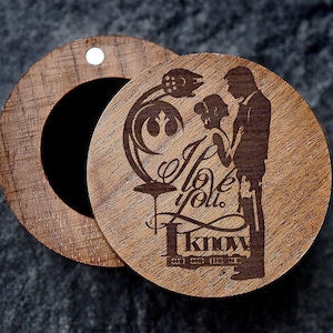 May include: A wooden ring box with a lid that has an engraved design of a couple standing in front of a Death Star. The text "I love you. I know." is engraved on the lid.