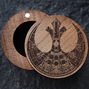 May include: A wooden box with a hinged lid. The lid features a laser-engraved design of the Rebel Alliance symbol from Star Wars. The symbol is a stylized X-wing starfighter.