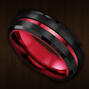 Puede incluir: Un anillo de carburo de tungsteno negro y rojo con un borde biselado y una incrustación roja.