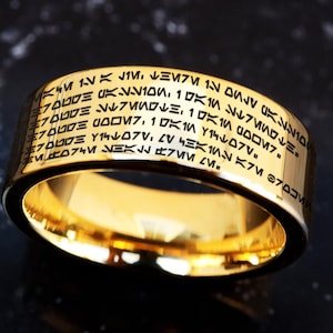May include: A gold ring with a black inscription in an alien alphabet. The inscription reads: "KM1VK JIM. DS 么么10 7000E UDOM7:11 イラレブV ブログ K100、1呎ロレミ フロロロミ Y140715 K7M 3プロUS M074M NEK".