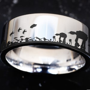 May include: A silver ring with a black band featuring a silhouette of Star Wars characters, including AT-ATs and X-wings.