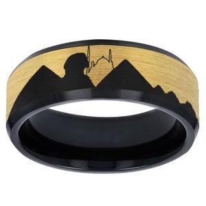 May include: Black tungsten carbide ring with a gold-toned band featuring a silhouette of a mosque and pyramids.