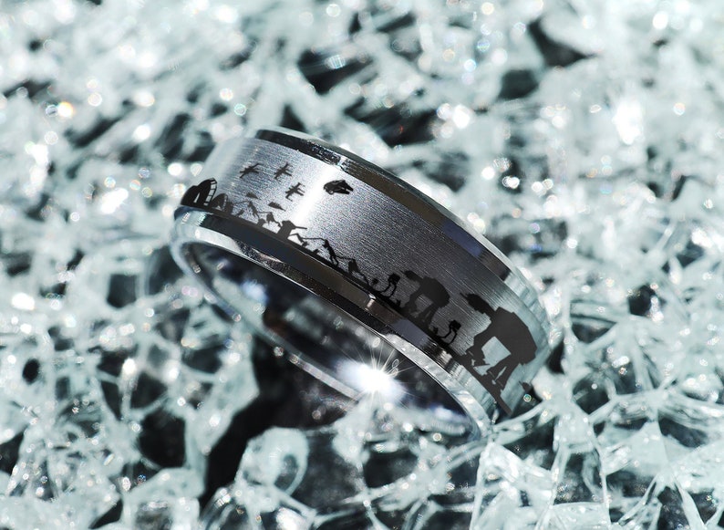 May include: A silver ring with a black band featuring a silhouette of the Millennium Falcon and other Star Wars characters.