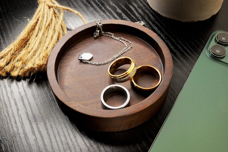 May include: A wooden ring dish with three rings, two gold and one silver, and a silver necklace with a heart pendant.