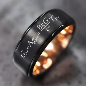 May include: A black tungsten carbide ring with a rose gold inner band. The ring is engraved with the Einstein field equation:  "Gμν + Λgμν = 8πGTμν / c4".