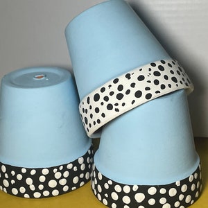 May include: Three light blue terracotta flower pots with a black and white polka dot design around the top rim.