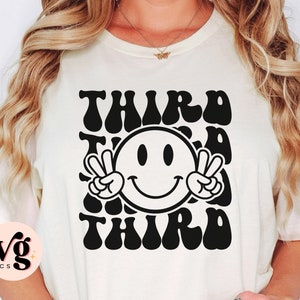 May include: White t-shirt with a black graphic design that says "Third Time's the Charm" with a smiley face in the middle.