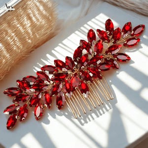 Puede incluir: Un peine decorativo para el cabello con un diseño floral adornado con piedras preciosas rojas brillantes. El peine tiene una base de metal dorado con múltiples dientes para sujetarlo al cabello. Las piedras preciosas son de forma ovalada.