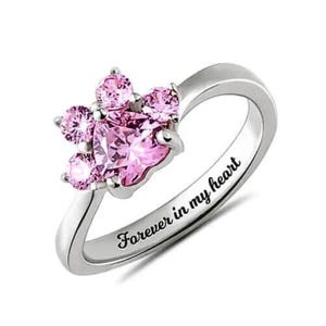 May include: A silver ring with a pink heart-shaped paw print design and the inscription "Forever in my heart".