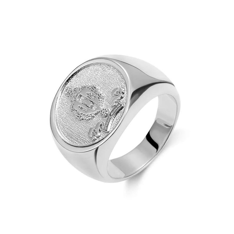 May include: A silver signet ring with a raised oval design featuring a crest and the word "Class" in a script font.