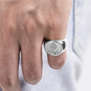 May include: A silver signet ring with a detailed crest design.