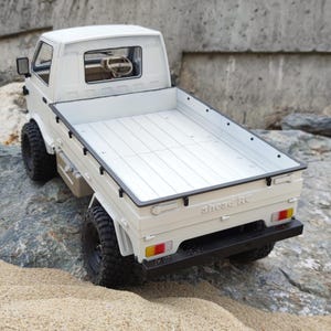 May include: White toy pickup truck with a flatbed, sitting on a rock. The truck has black tyres and a black bumper.