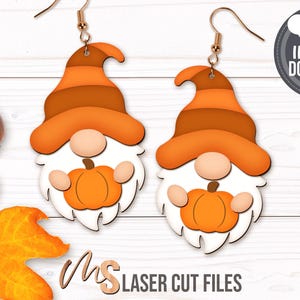 May include: A pair of orange and brown gnome earrings with a pumpkin in each hand. The earrings are made of wood and are ready to be laser cut.