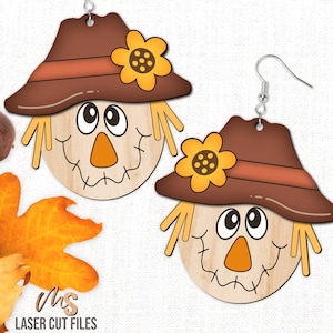 May include: A pair of wooden cutout earrings featuring a scarecrow face with a brown hat and a yellow sunflower. The earrings are designed for fall or autumn decor.